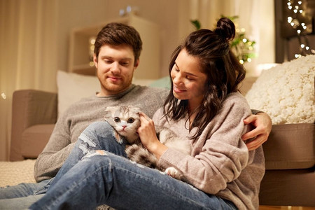 宠物，hygge和人的概念—快乐的夫妇与猫在家里。快乐的夫妇与猫在家里