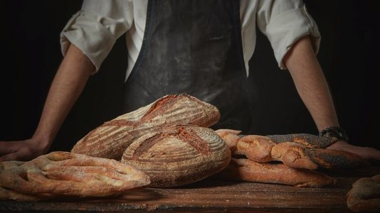 面包师与新鲜面包在木棕色桌子背景。新鲜面包在桌子上