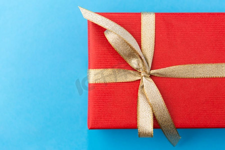 金色蝴蝶结摄影照片_节日，问候和惊喜概念-圣诞红色礼盒，蓝底金色蝴蝶结。蓝色背景的圣诞红色礼盒