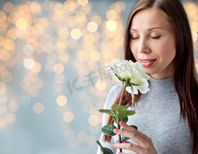 人与花的概念-快乐的年轻女子在节日灯光下闻着大白玫瑰的味道。节日灯光下散发着白玫瑰气息的女人