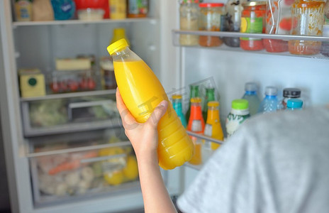春风十里菜单摄影照片_十几岁的女孩从开着的冰箱里拿出橙汁。十几岁的女孩从冰箱里拿出橙汁
