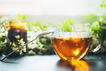 蜂蜜主图1摄影照片_一杯新鲜的蜂蜜凉茶放在木桌上，上面有绿色的树枝和花朵，俯瞰。选择性聚焦，水平。