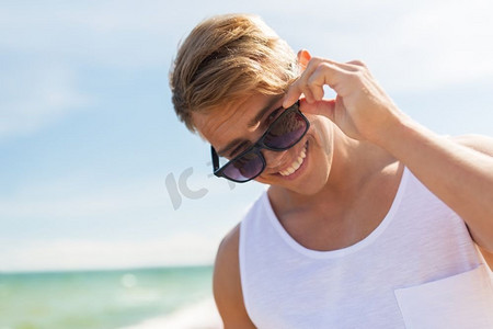 暑假和人概念-太阳镜的愉快的微笑的年轻人在海滩。微笑的年轻人在太阳镜在夏天海滩