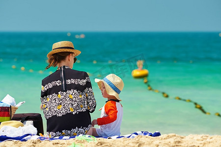 孩子和母亲摄影照片_两岁的男孩戴着太阳帽和母亲在海滩上