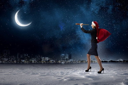 圣诞节就要到了。穿着正式西装，戴着圣诞帽的女人看着望远镜