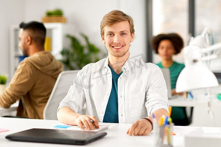 企业和人的概念—愉快的微笑男性创造性工作者与笔记本电脑坐在办公桌。男性创意工作者与笔记本电脑在办公室