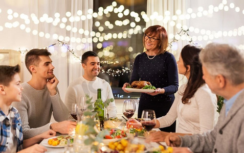 海天盛宴摄影照片_庆祝，节假日和人的概念-幸福的家庭在家里吃烤鸡作为晚餐。幸福的一家人在家里吃晚餐