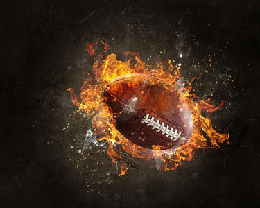足球联赛展板摄影照片_橄榄球在火火焰在黑暗背景。混合媒体。美式足球游戏概念混合媒体