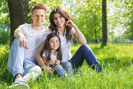 公园里幸福的一家人的肖像。阳光明媚的一天，幸福的一家人坐在公园的树下草地上