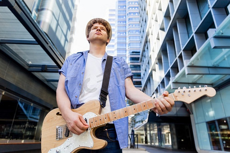 弹吉他的人摄影照片_城市里弹吉他的年轻音乐家。城市里拿着吉他的年轻音乐家的肖像