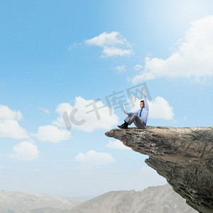 生意兴隆。一位年轻的商人坐在岩石山边，用着平板电脑