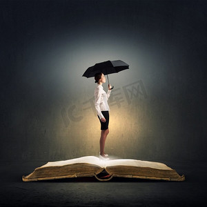 撑着伞的女人。一位年轻的女商人，撑着一把黑色的雨伞站在书上