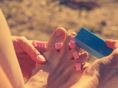 在海滩上度假期间做修脚的不可识别的妇女。女性用分离器打磨她的脚指甲。女子足疗户外