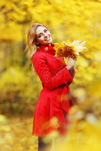 美女拿叶摄影照片_一位年轻的美女拿着一束枯叶在秋天的公园里摆姿势