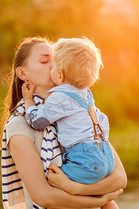 阳光开心摄影照片_快乐的女人和孩子在户外玩得开心。家庭生活方式，夕阳下母子俩的田园风光。男孩在亲吻他的妈妈。