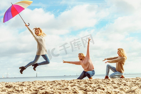 三个点摄影照片_三个充满欢乐的女人拿着五颜六色的伞跳来跳去。女性朋友有乐趣户外。带着雨伞跳的女人