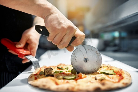 食物，意大利厨房和烹饪概念-在披萨店用切刀将披萨切成碎片。在披萨店做饭把披萨切成碎片