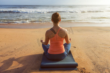 做瑜伽的妇女—冥想和放松在Padmasana莲花姿势户外在日落的热带海滩。妇女做瑜伽莲花姿势户外在海滩