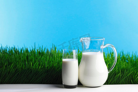 草地上的牛奶罐和玻璃杯。鲜绿的草地背景上的牛奶壶和玻璃