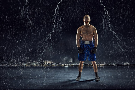实力展示摄影照片_拳击手在户外训练。黑色背景下的强壮拳击手展示了力量和耐力