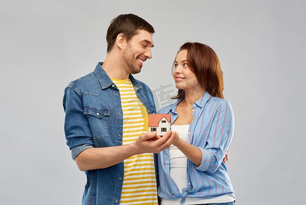 房地产、家庭和抵押概念—微笑的夫妇持有房子模型在灰色背景。微笑的夫妇举行房子模型