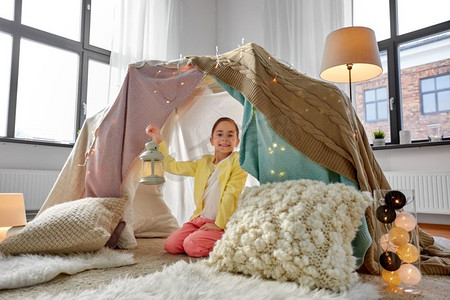 童年和hygge概念—有灯笼的快乐的小女孩在孩子帐篷或帐篷在家里小女孩与灯笼在孩子们帐篷在家里