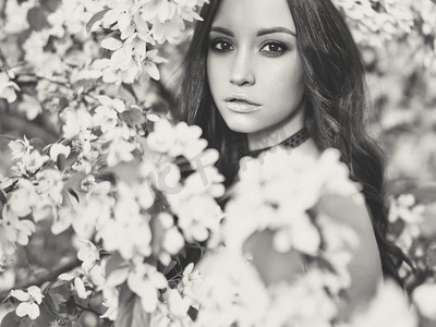 花朵黑白摄影照片_美丽的年轻女子被苹果树的花朵包围的黑白户外时尚照片。春暖花开。夏日氛围