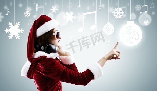 庆祝新年。年轻漂亮的圣诞老人女孩戴着耳机听音乐