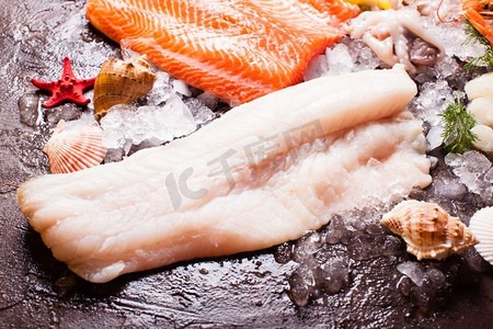 清酒煮蛤蜊摄影照片_冰上的海鲜，在棕色石板背景上靠近的鳕鱼片。冰上海鲜