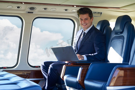 飞行中在直升机舱内用笔记本电脑工作的商人肖像