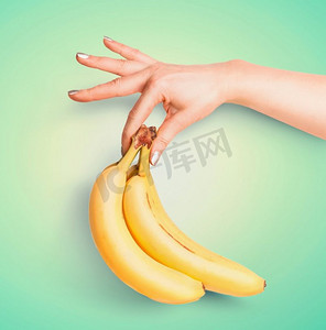 青绿色背景下，女性手中拿着一串有机香蕉。夏季热带水果概念。为您的设计复制空间