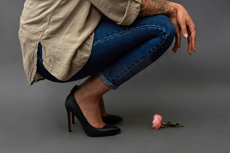 穿着牛仔裤的年轻时尚女孩蹲着,手里拿着粉红色的花,背景是深色,有
