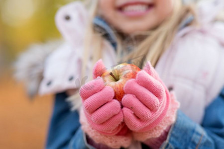 童年，季节和自然概念—小女孩拿着苹果在秋天的特写镜头。关闭的小女孩拿着苹果在秋天