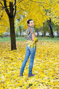 跑了摄影照片_秋天的公园里，一位微笑的成年白人妇女带着黄色的枫叶跑了。