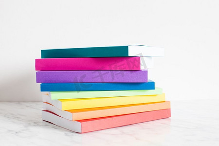 彩色书籍以彩虹的颜色勾勒出轮廓。把书堆在白墙附近的书架上。五颜六色的藏书