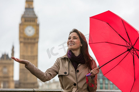 快乐大本营摄影照片_拿着红色雨伞的女孩或年轻女子，伸出手，在大本钟附近寻找雨点，英国伦敦