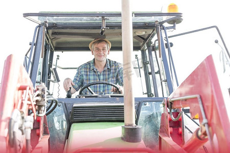 拖拉机的人摄影照片_自信的成熟农民驾驶拖拉机的肖像在农场