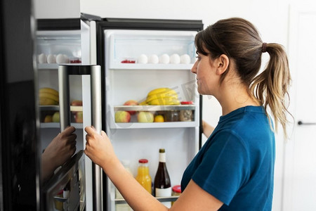 健康的饮食，食物和饮食概念—妇女在开放冰箱在家庭厨房。女人在打开冰箱在家庭厨房