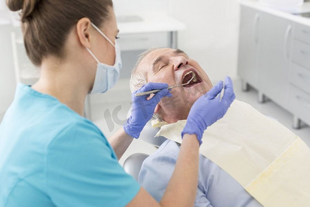 牙科医生在治疗中用斜镜和刮刀检查老年患者的口腔