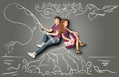 一对笔画摄影照片_幸福的情人节爱情故事概念：一对浪漫的情侣坐在岛上，在粉笔画的背景下，在钩子上钓鱼一条金鱼。