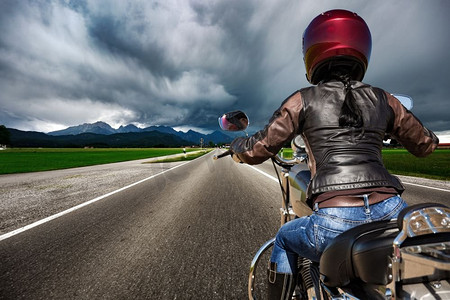 一名骑摩托车的女孩在闪电风暴中疾驰在路上--德国巴伐利亚州福根塞和施万高