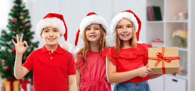 圣诞节,假期和童年的概念-微笑的小孩在圣诞老人助手帽子与礼品盒显示