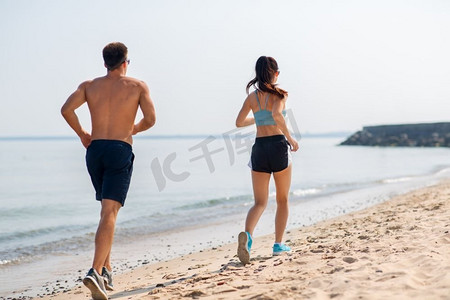 健身、运动和生活方式理念-快乐的情侣沿着夏季海滩跑步。一对身着运动服的夫妇在海滩上奔跑