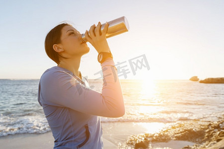 一名妇女在海滩上喝水。年轻女子在海滩上运动后喝水