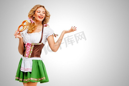 吃卷饼摄影照片_美丽的啤酒节女人穿着传统的巴伐利亚连衣裙，手里拿着椒盐卷饼，背景是灰色。