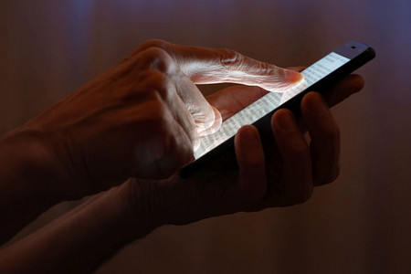 小窗帘摄影照片_晚上，一名男子在拉上窗帘的窗户附近用手指在黑色智能手机的触摸屏上打字