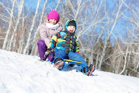 玩雪橇的孩子摄影照片_冬天的乐趣。男孩和女孩在美丽的雪地公园玩雪橇