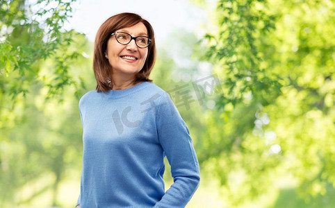 视觉与老人概念--戴着眼镜的老年女性在绿色的自然背景下微笑。戴眼镜的资深女性超越自然背景