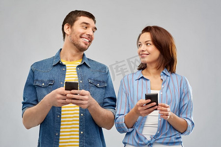 技术和人的概念—愉快的夫妇与智能手机谈话在灰色背景。幸福的夫妇与智能手机交谈