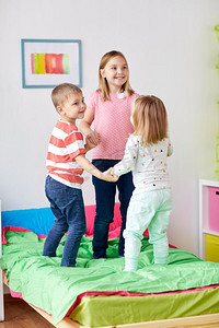 童年，休闲和家庭概念-快乐的小孩子在家里的床上跳。快乐的小孩子们在家里的床上跳着